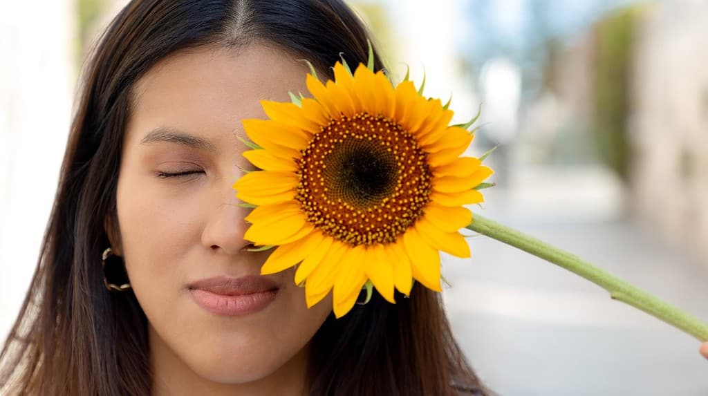 Young woman, smiling and holding a sunflower on a sunny spring day in a park, selective focus, concept of joy and blossoming in spring. Peace, giant and yellow sunflowers.