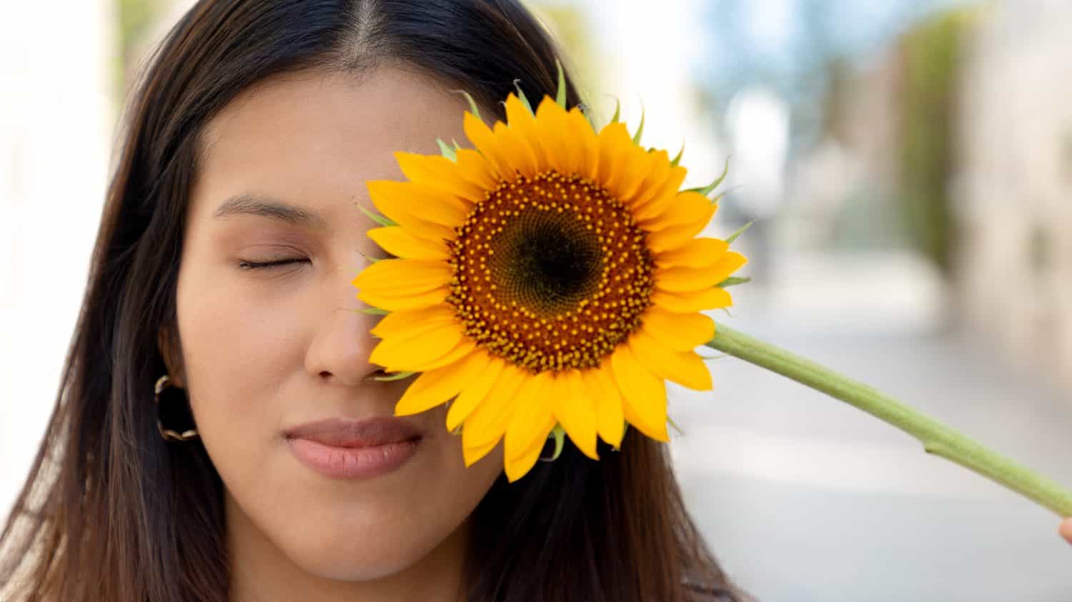 Young woman, smiling and holding a sunflower on a sunny spring day in a park, selective focus, concept of joy and blossoming in spring. Peace, giant and yellow sunflowers.