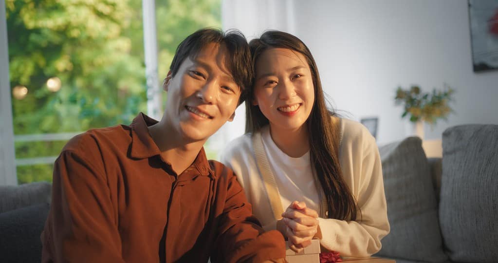 Lovely South Korean Couple Having a Birthday Celebration. Young Man Gifting a Present to His Beautiful Partner. Happy Boyfriend and Girlfriend Gently Smiling and Looking at Camera