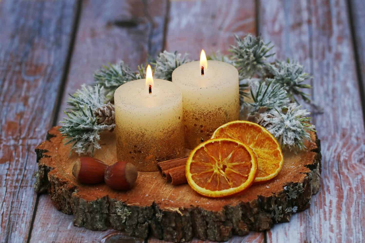 Christmas and Advent decoration candles with branches, nuts. Orange slices and cinnamon stick arranged on a tree slice.