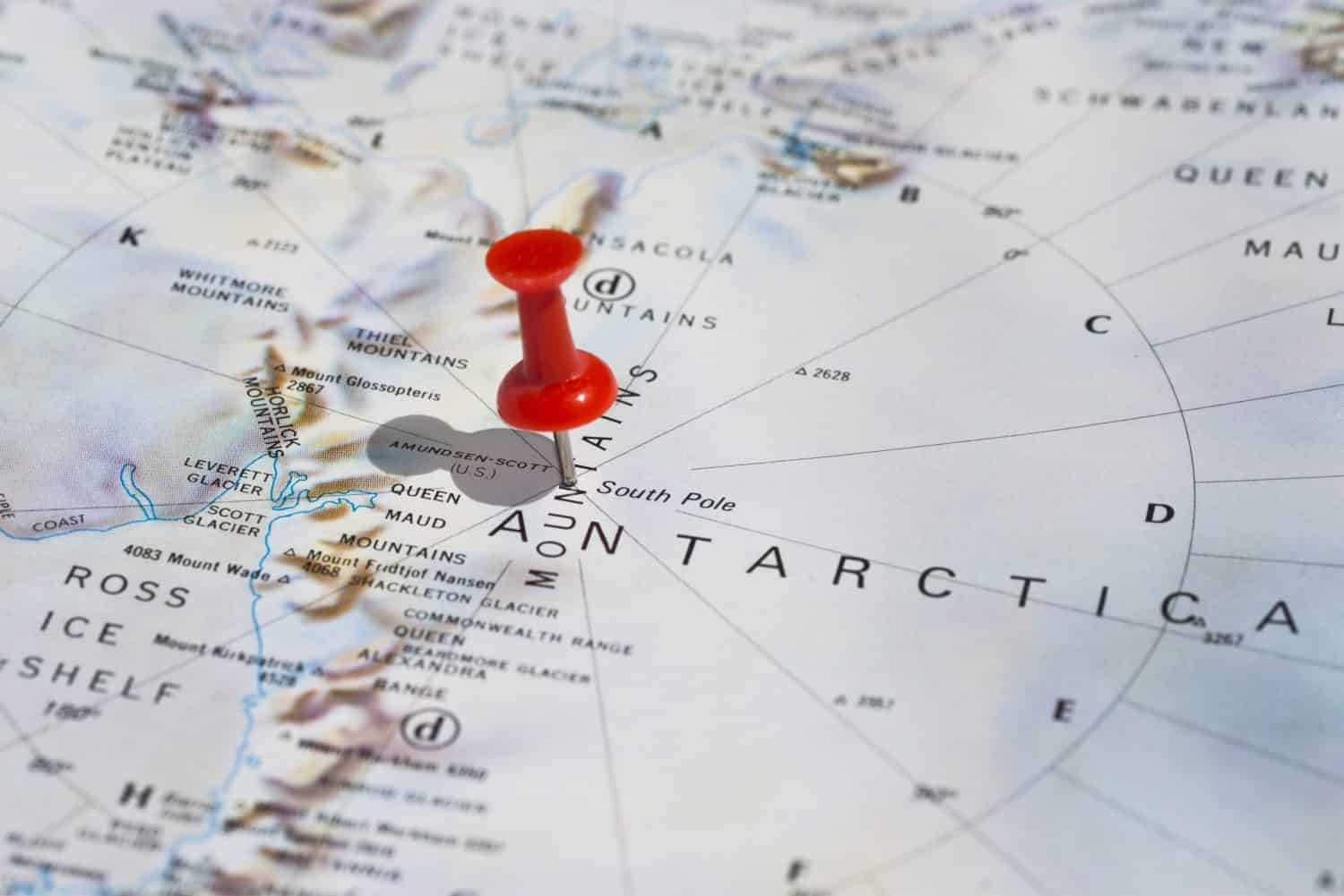 South Pole marked on map with red pushpin. Selective focus on the word South Pole and the pushpin. Pin is in an angle and casts some shadow to the left. 