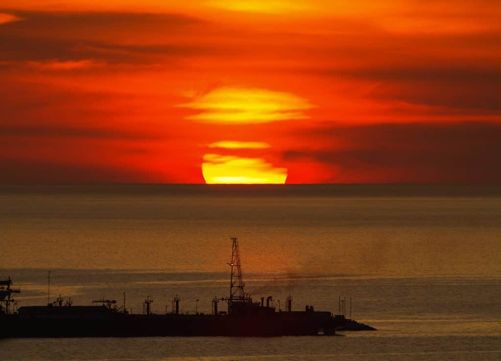 Big round sunset hiding behind the clouds over the horizon on Gulf of Mexico (from Mexico Campache) with silhouette of a big ship