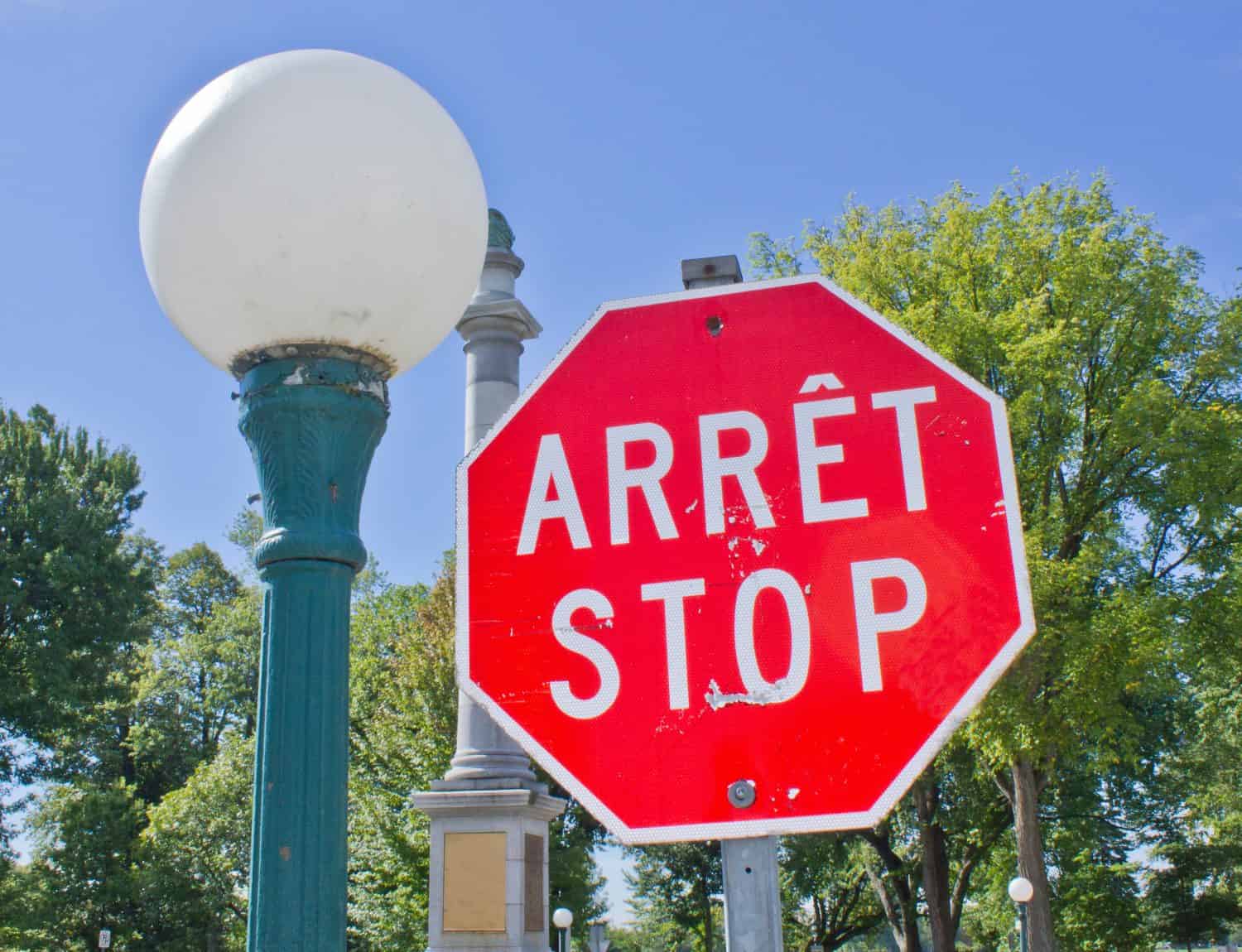 A bilingual French and English, red and white stop sign beside a classic lamp post at the entrance to a park in Quebec City, Canada.