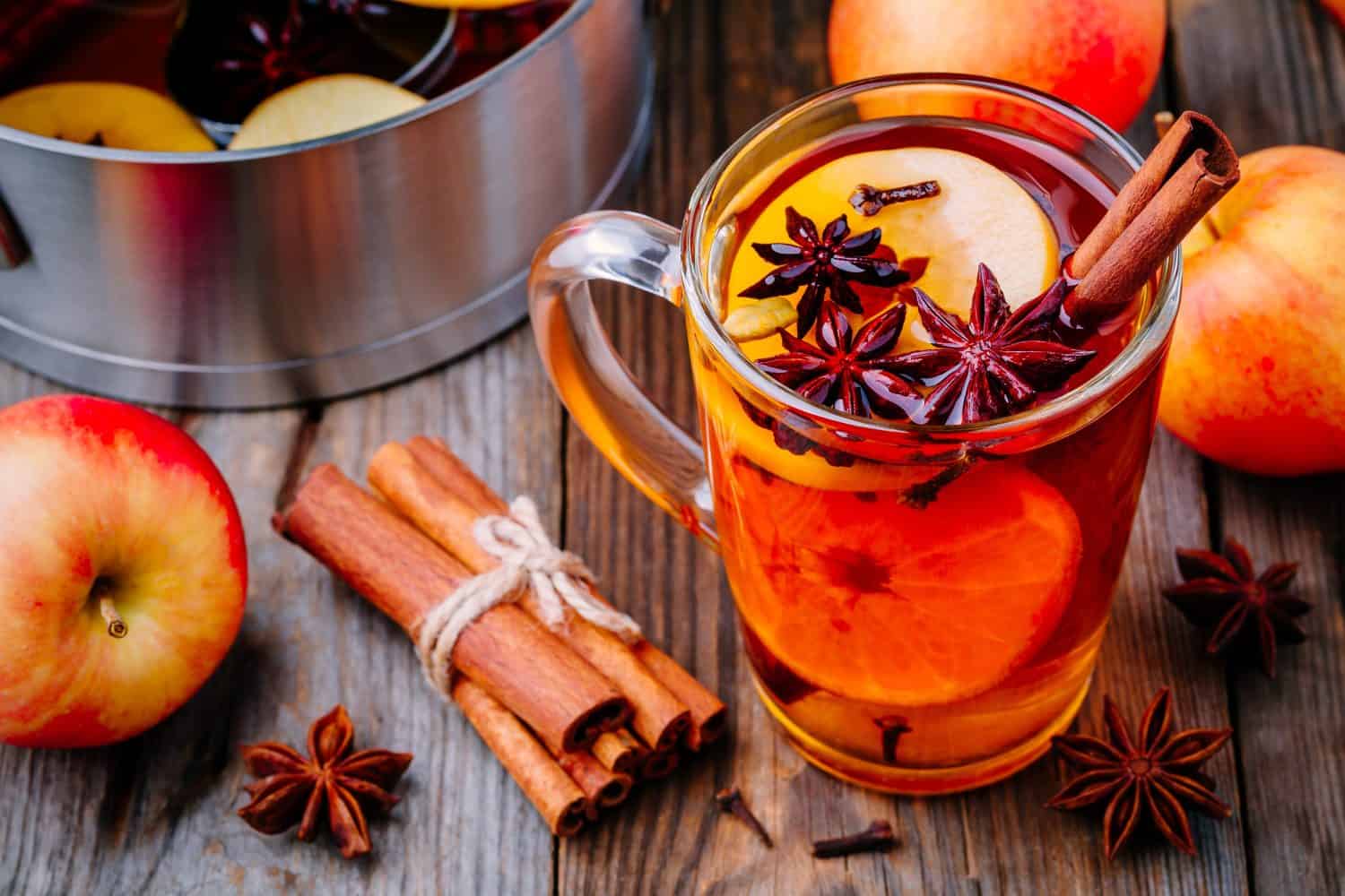 Hot mulled apple cider with with cinnamon sticks, cloves and anise on wooden background