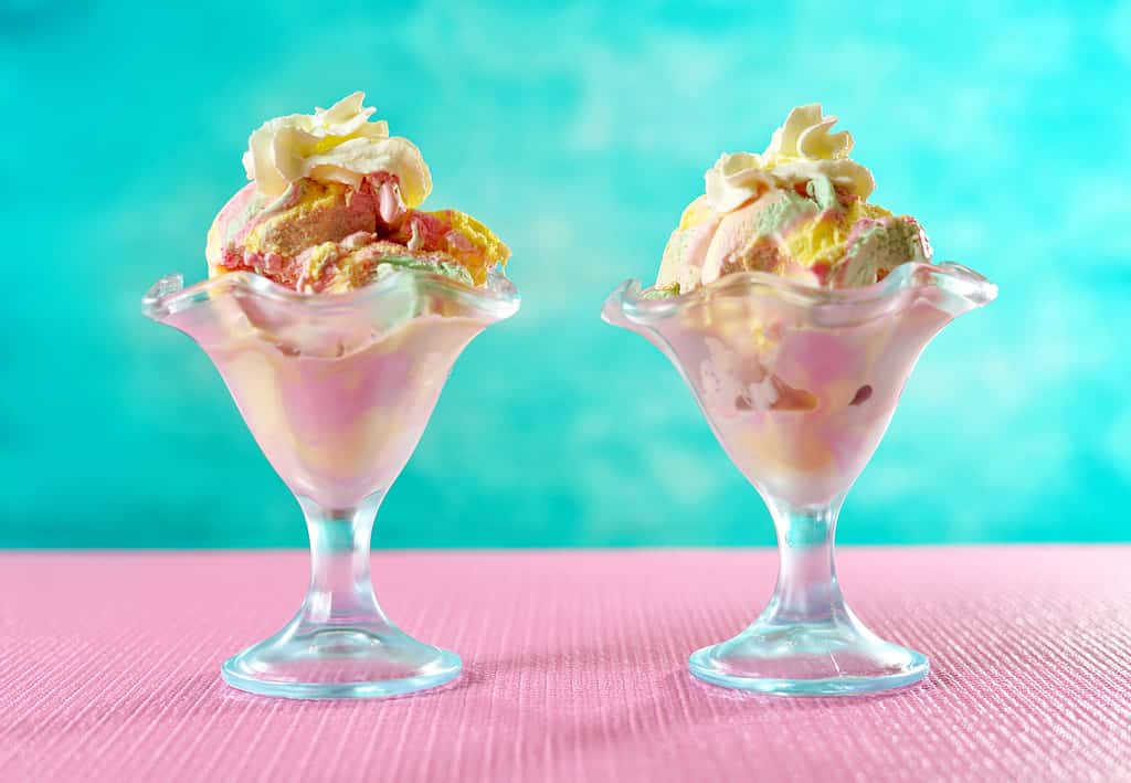 Rainbow ice cream in sundae glasses on bright colorful background.