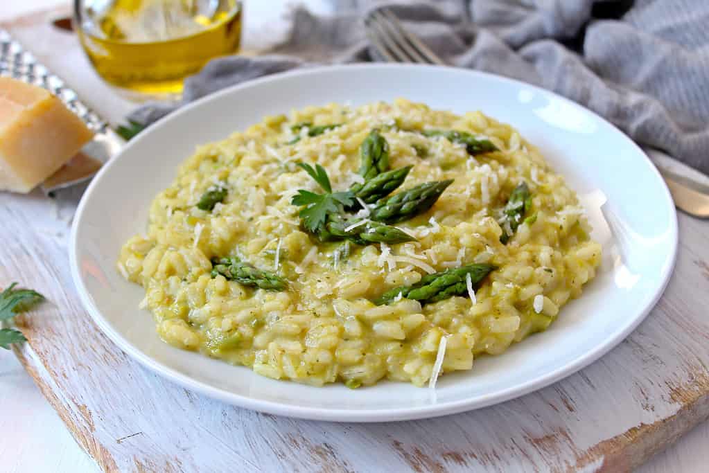 Italian risotto with spring asparagus and parmesan cheese in plate on light background.