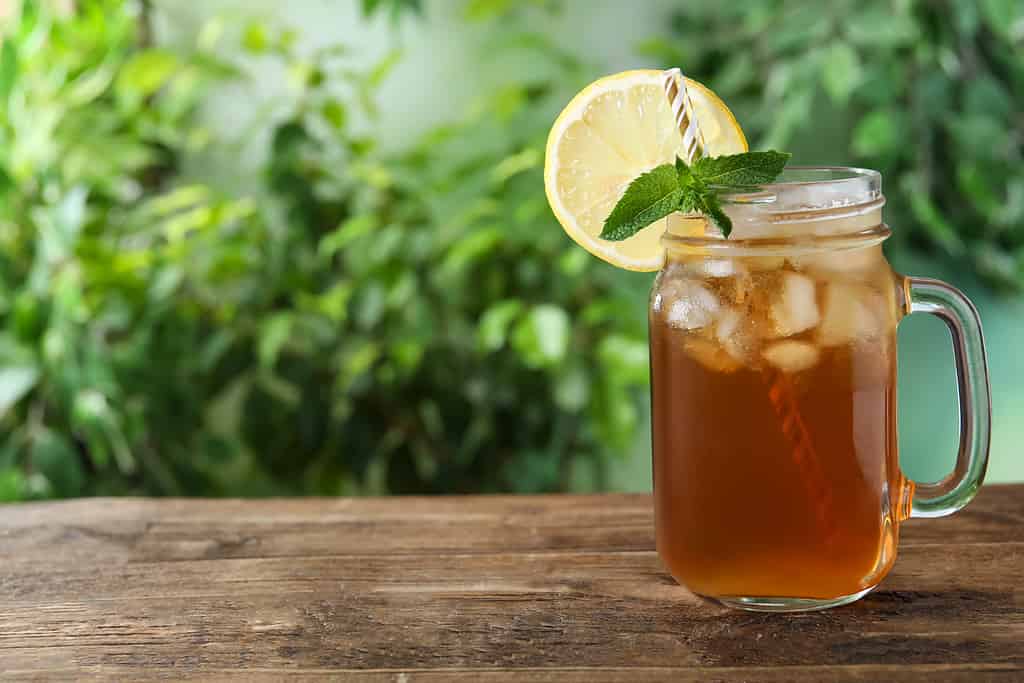 Delicious iced tea in mason jar on wooden table outdoors, space for text