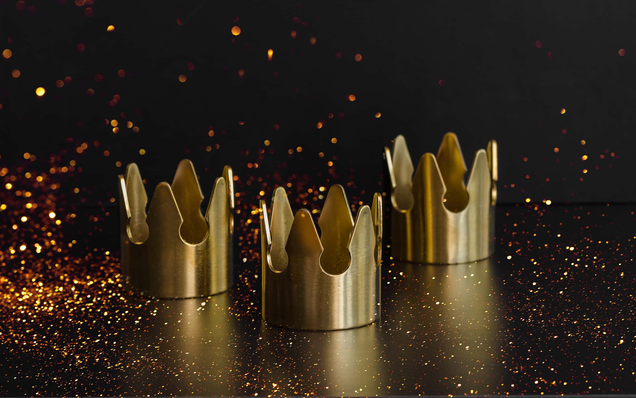 Epiphany Day or Dia de Reyes Magos concept. Three gold crowns on black background with golden particles.