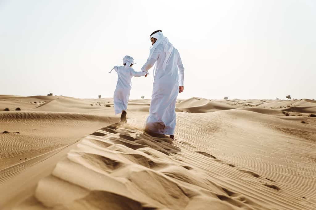 Middle-eastern father and son wearing arab traditional kandura spending time in the desert, Dubai