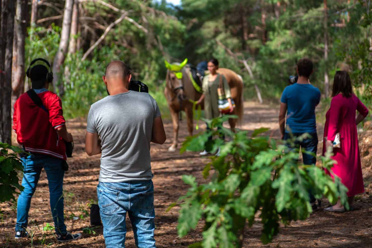 Filmmaking team in forrest doing their job - making video with blurred girl and a horse on the back