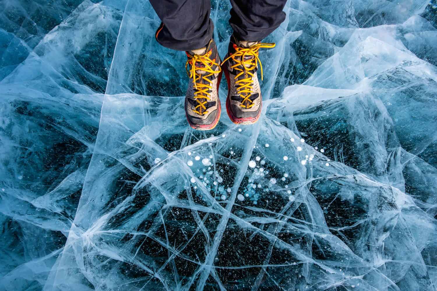 Traveller man foot standing on cracks surface of the natural ice in frozen water at Olkhon Island, Baikal lake, Russia
