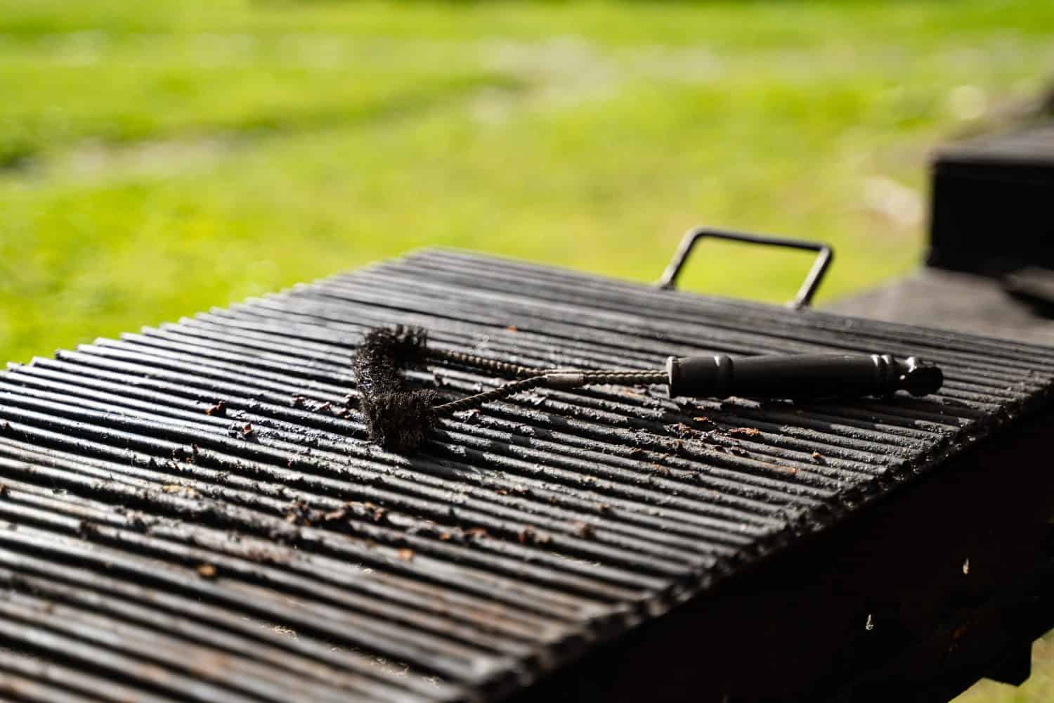 front view closeup of outdoor empty barbeque grill with black brush tool for cleaning on top in outdoor setting with green grass