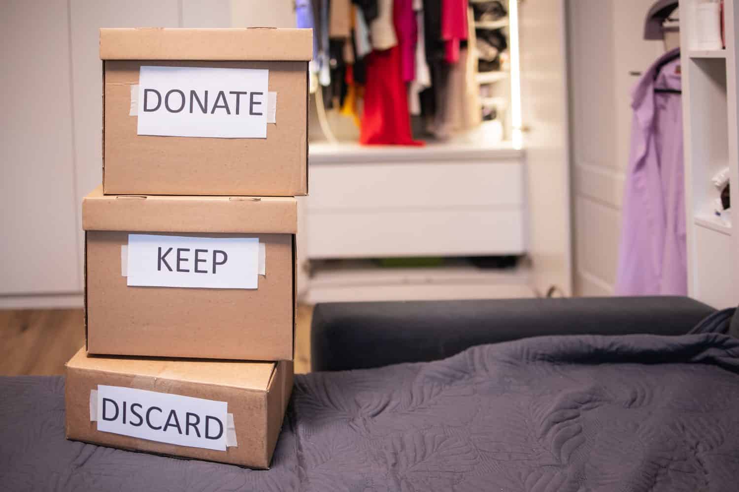 No people clothes are sorting into three boxes that stand on top of each other against the backdrop of an open minimalist wardrobe. Concept: minimalism, decluttering, charity, reuse zero waste
