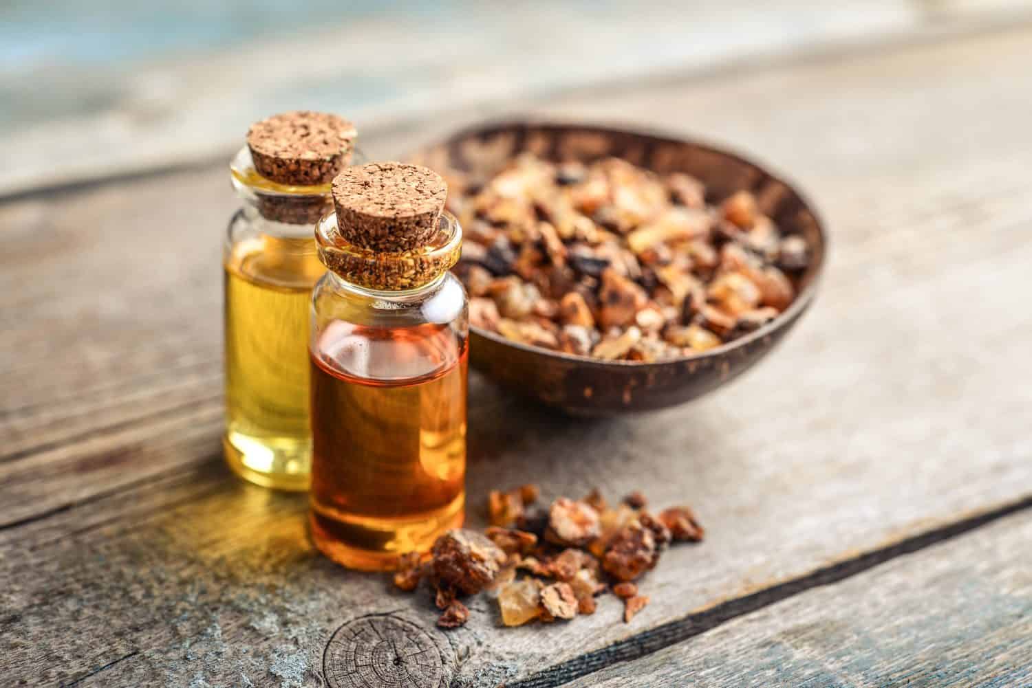 A bottle of myrrh essential oil with myrrh resin on a wooden background
