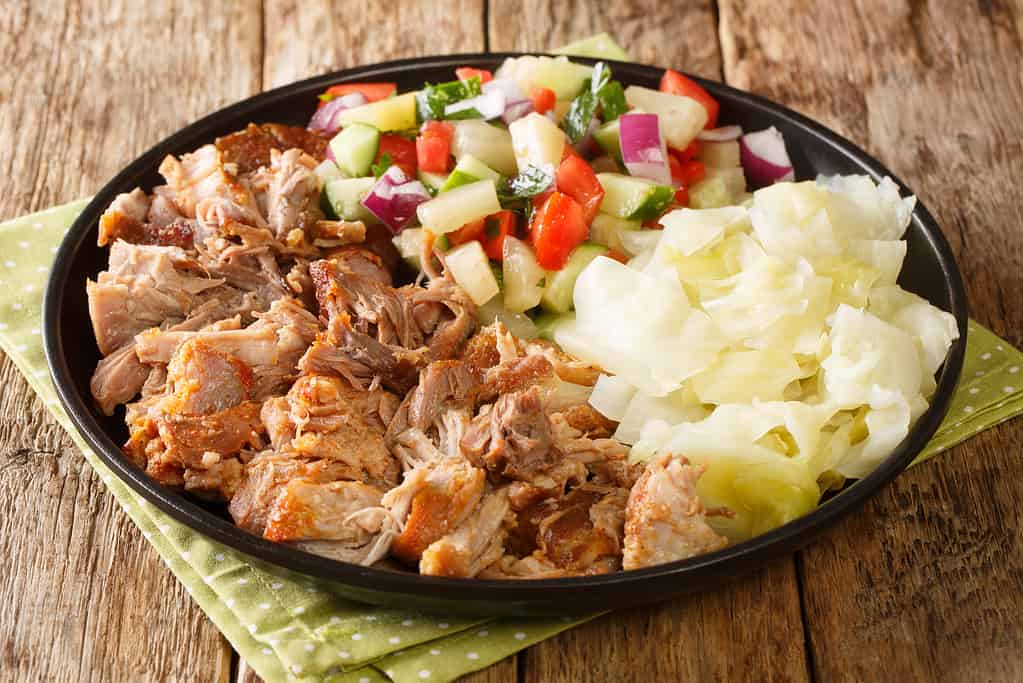 Hawaiian Kalua Pork with stewed cabbage and fresh salad close-up in a plate. horizontal