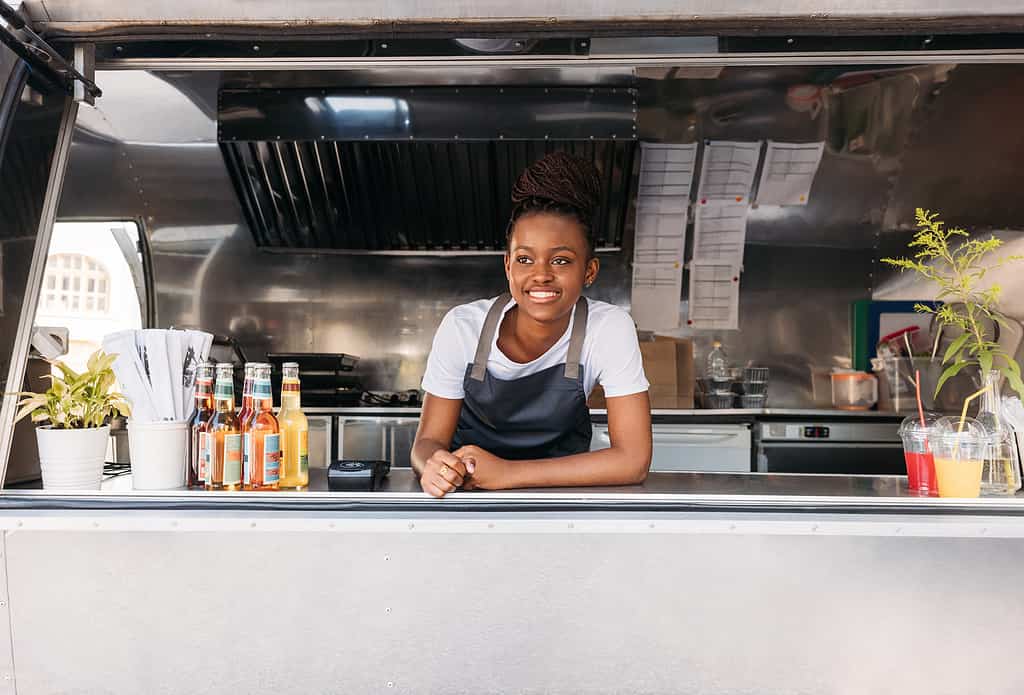Portrait of young saleswoman waiting for clients. Food truck owner leaning on a counter looking away.