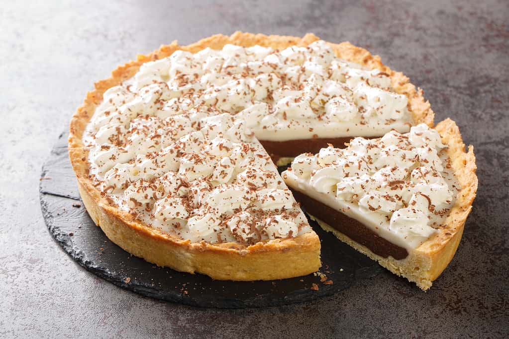 Chocolate Haupia Pie is a creamy coconut custard pie in a flaky pie crust and topped with whipped cream closeup in the plate. Horizontal