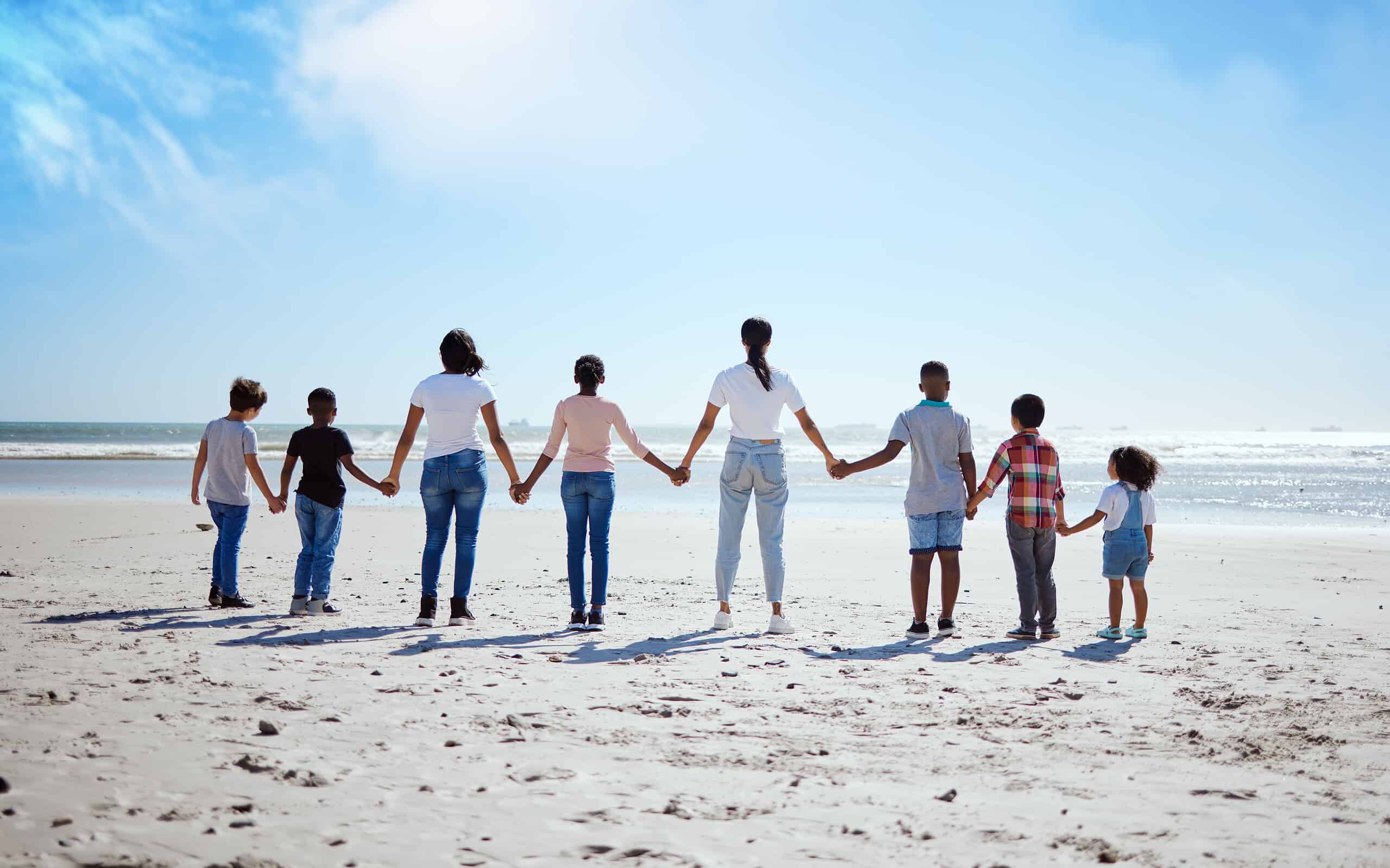 Support, back and big family holding hands at the beach, summer walking and travel holiday in nature of Portugal. Hope, love and women with affection for adopted kids on a vacation at the ocean