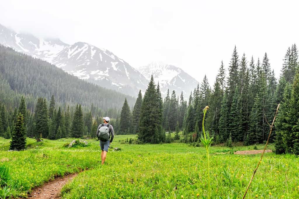Open valley with man hiker walking in rain on Conundrum Creek Trail in Aspen, Colorado in 2019 summer on cloudy day and dirt road