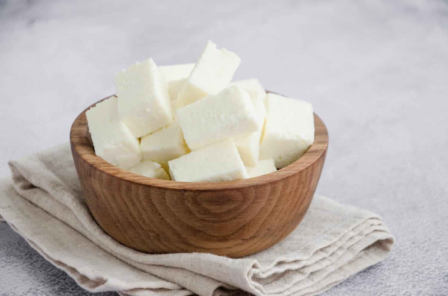 Homemade Indian paneer cheese made from fresh milk and lemon juice, diced in a wooden bowl on a gray stone background. Horizontal orientation. Close up