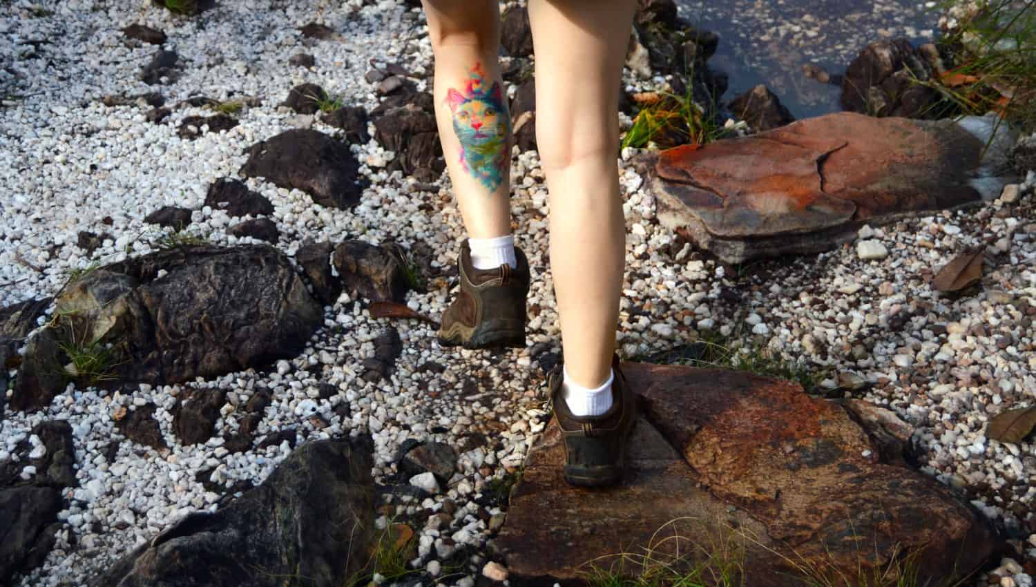 Woman with a watercolor cat tattoo on her leg hiking a stone path