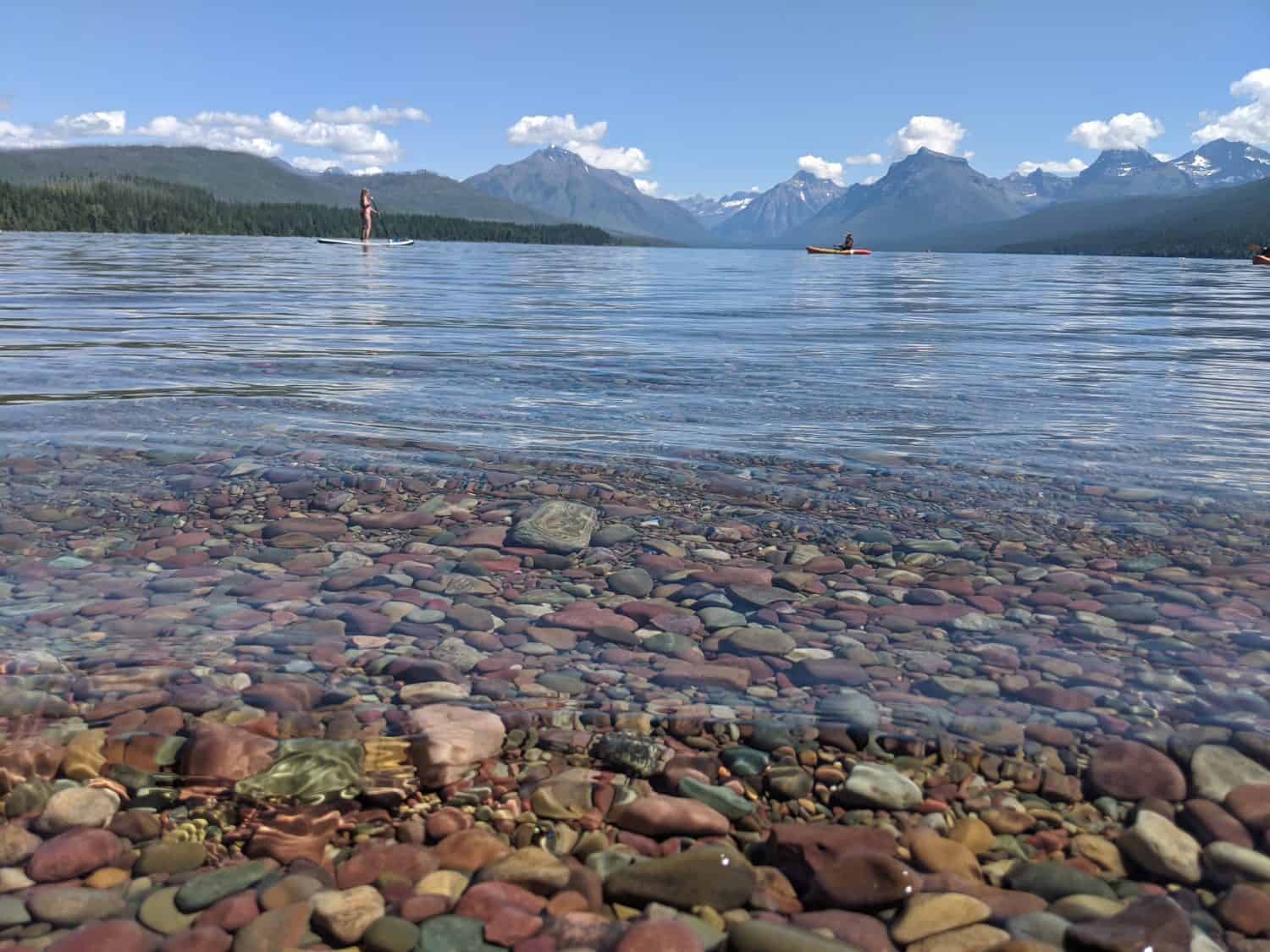 The colorful rock shore of Lake McDonald in Glacier National Park looking at the mountains. 