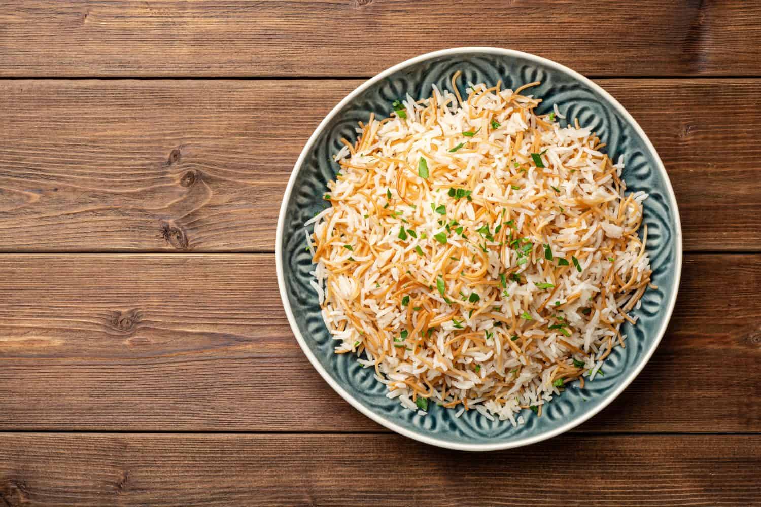 Rice with vermicelli in plate on wooden background. Traditional arabic dish. Top view, copy space.