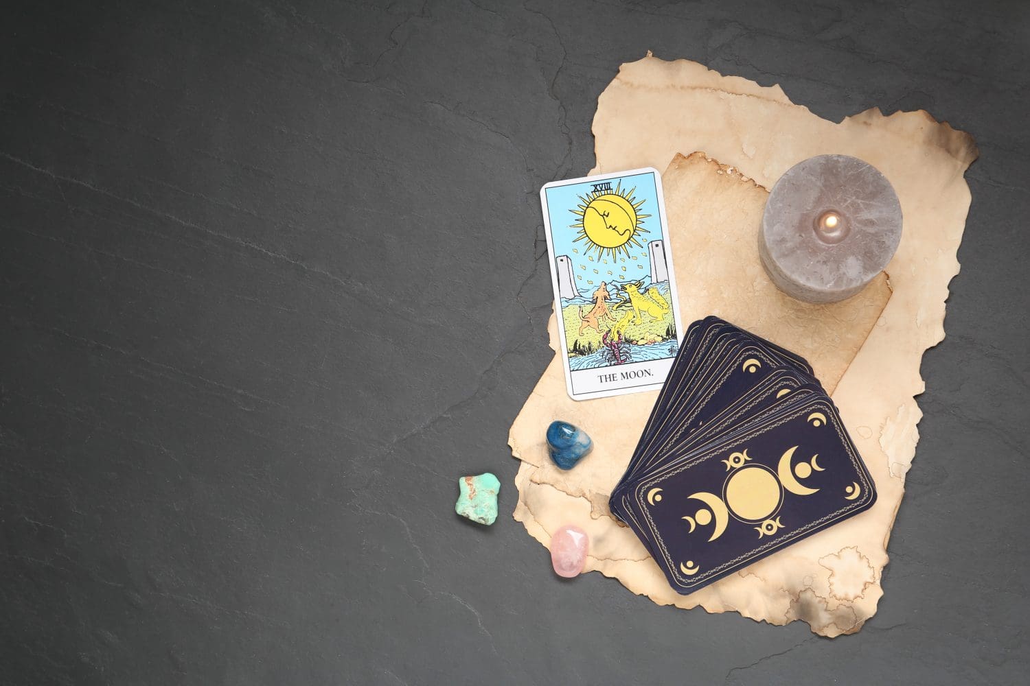 The Moon with other tarot cards, candle and gemstones on black table, flat lay. Space for text
