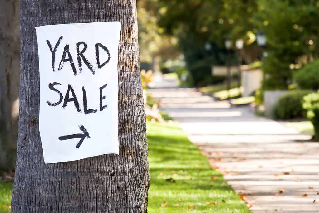 Hand painted paper yard sale sign with direction arrow stapled to a palm tree.