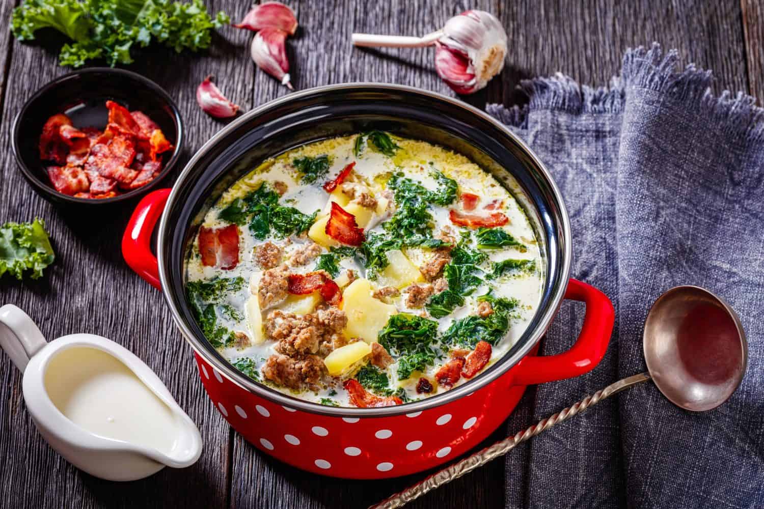Zuppa Toscana, hearty Tuscan Soup loaded with Italian sausage, kale, bacon and potatoes in red pot on dark wooden table