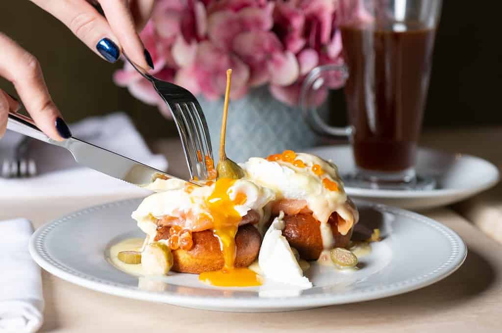 Girl eating eggs benedicts with smoked salmon, capers and salmon caviar for breakfast
