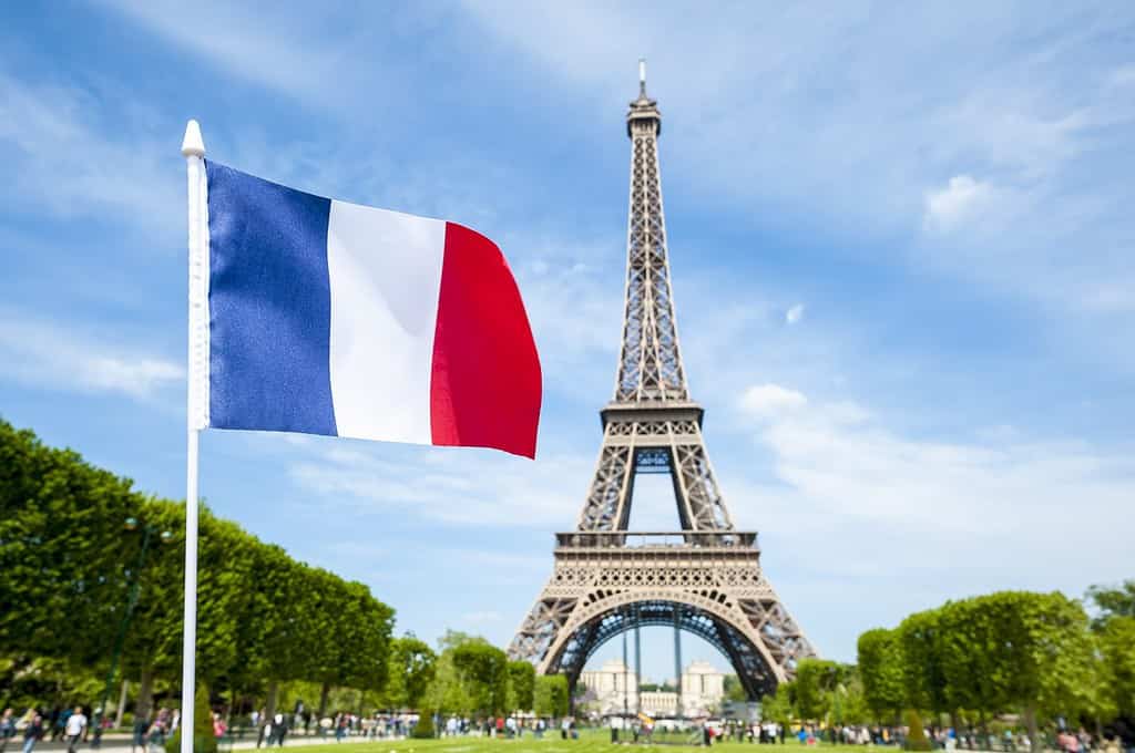 French flag flying in bright blue spring sky in front of the Eiffel Tower in Paris, France