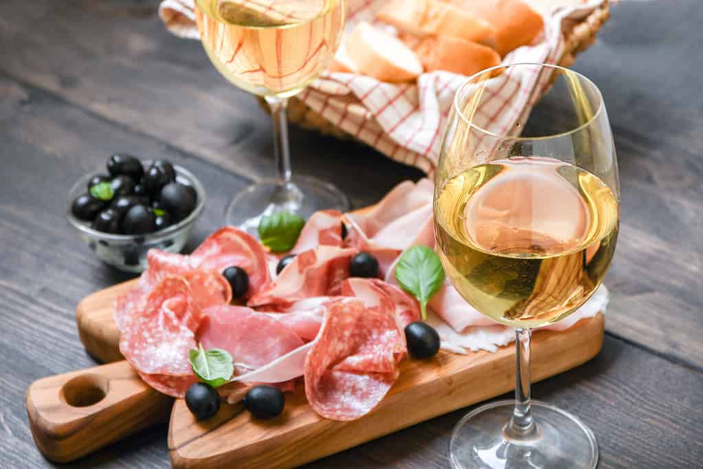 Food antipasto prosciutto ham, salami, olives and bread sticks. Charcuterie board. Two glasses of white wine or prosecco