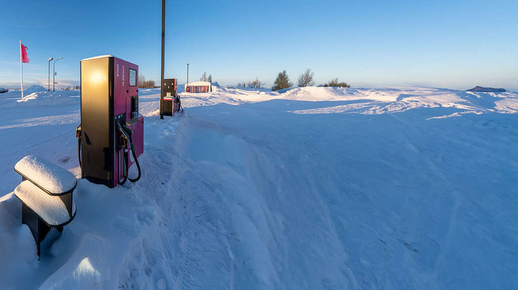 Petrol and diesel pump surrounded by snow and illuminated by morning sunlight at a service station in Iceland after a heavy snowfall