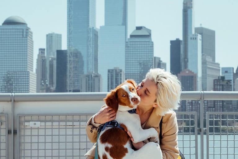 Pretty blond hipster girl walking cute dog in the city with skyline background.