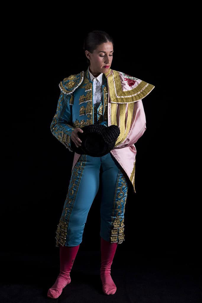 Woman bullfighter with blue costume back on black background
