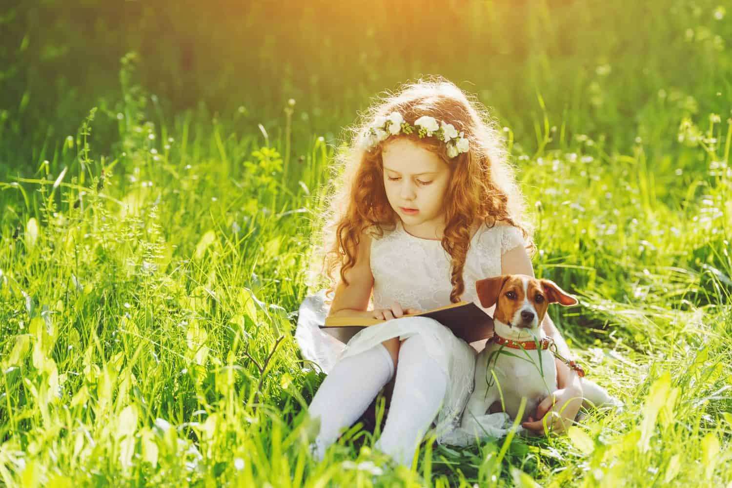 Little girl reading a book with her friend puppy dog in the outdoors.