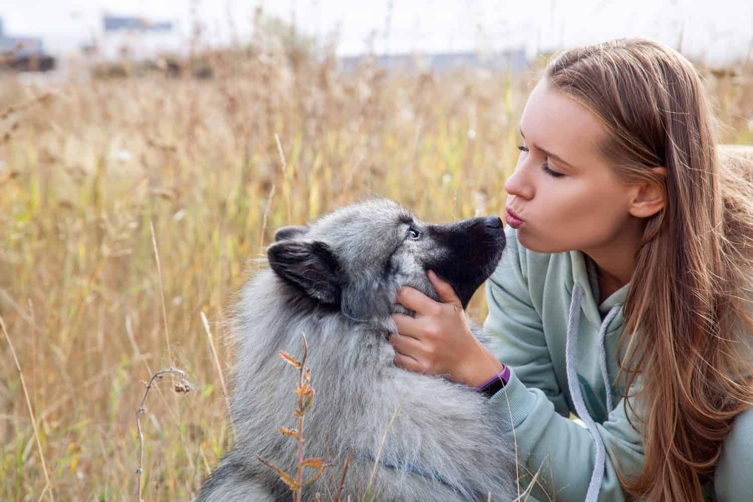 Young woman with her dog hugging and kissing in the field.