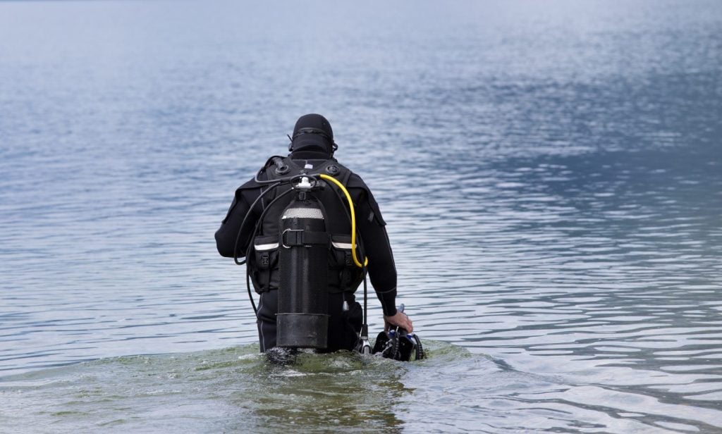 Diver with full equipment entering water in mountain lake
