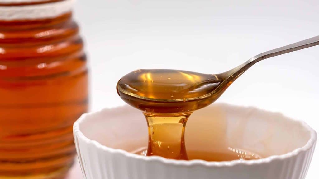 Fresh pure honey in a glass bowl with a honey dripper on the wooden tray.