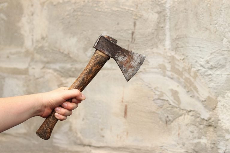 An ax in female hands on a blurred wall background. Old ax with rust close-up. Hand tools for repair and construction. Close-up of an ax in a woman's hand