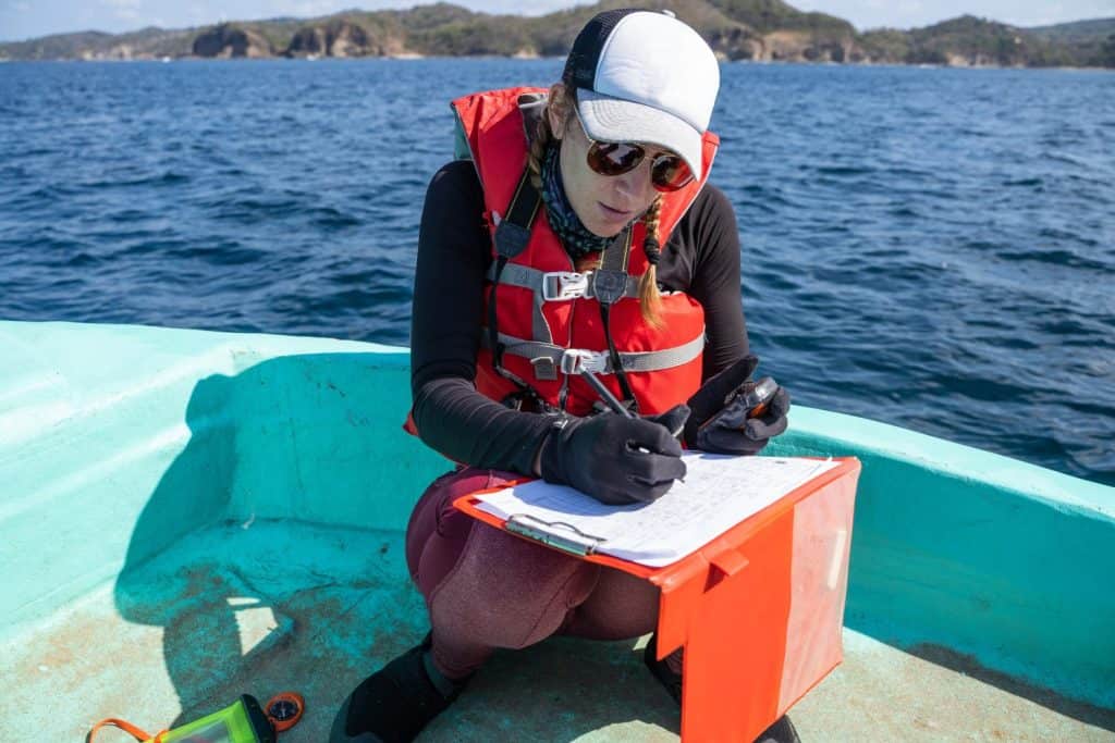 Equipped marine biologist writing notes on a paper while working on a boat
