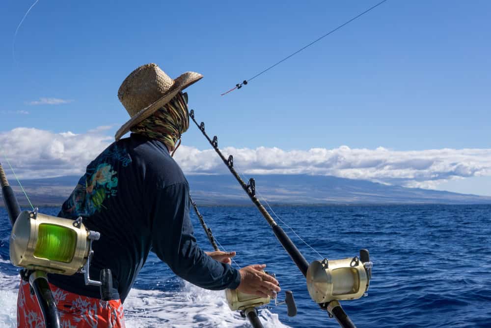 Big Island, Hawaii, USA. Male fishing on a boat. Fishing trip while on vacation. Deep blue water, nice sky. Action shot.
