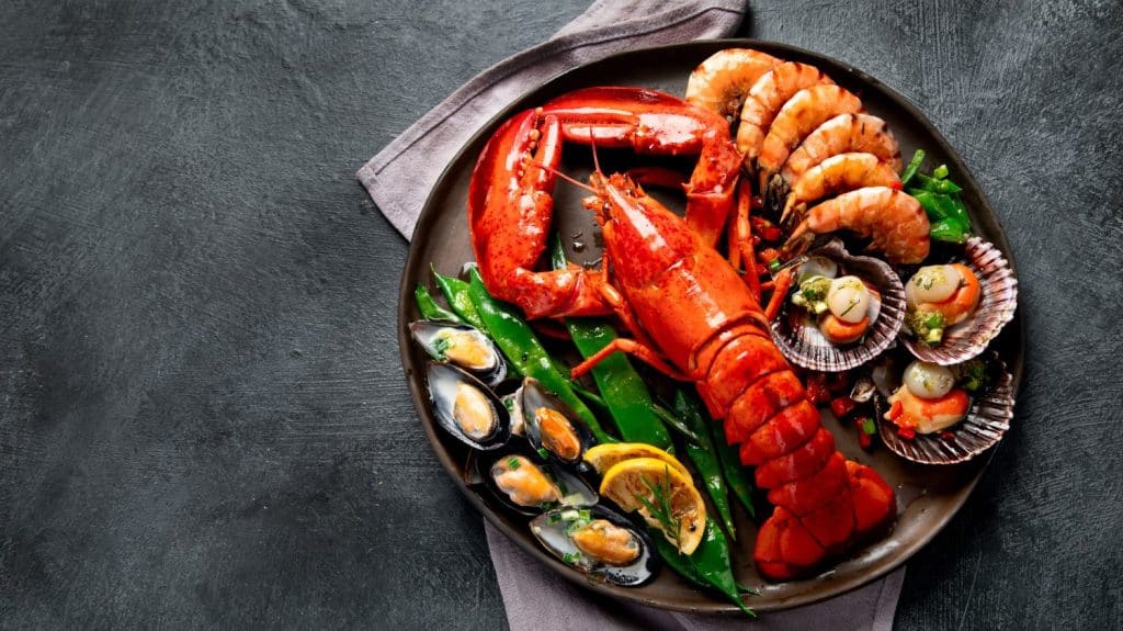 Big red lobster on plate with shrimp and mussels with lemon, souce pesto and bread. Seafood concept. Top view, copy space