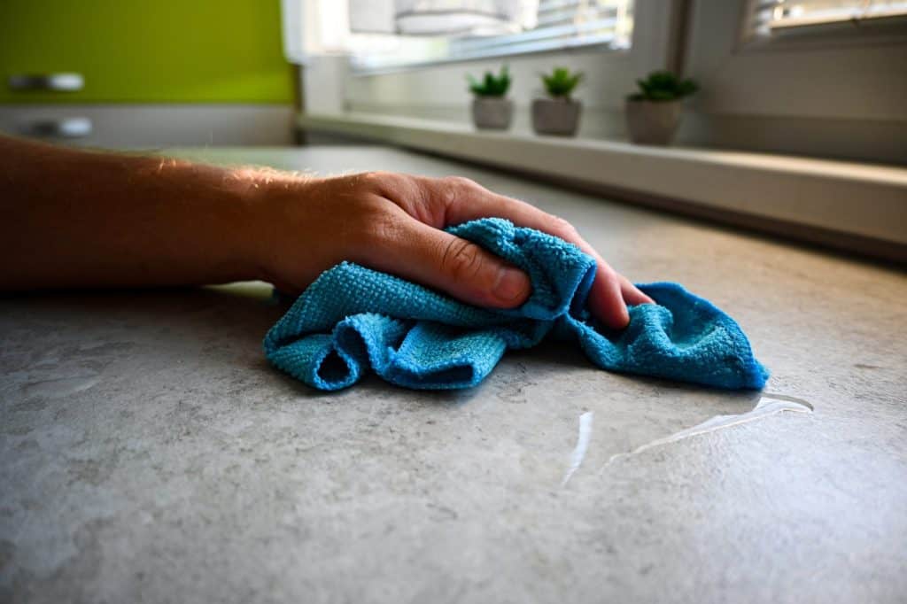 Person is wiping up a spill on a kitchen counter with a blue microfiber cloth.