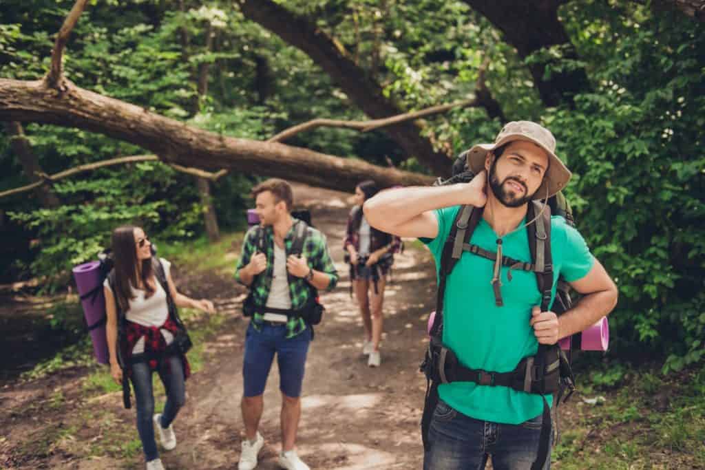 Hard, difficult, tiring and exhausting expedition of four friends in wild forest in trail. Guy is struggling of a neck pain, massaging it