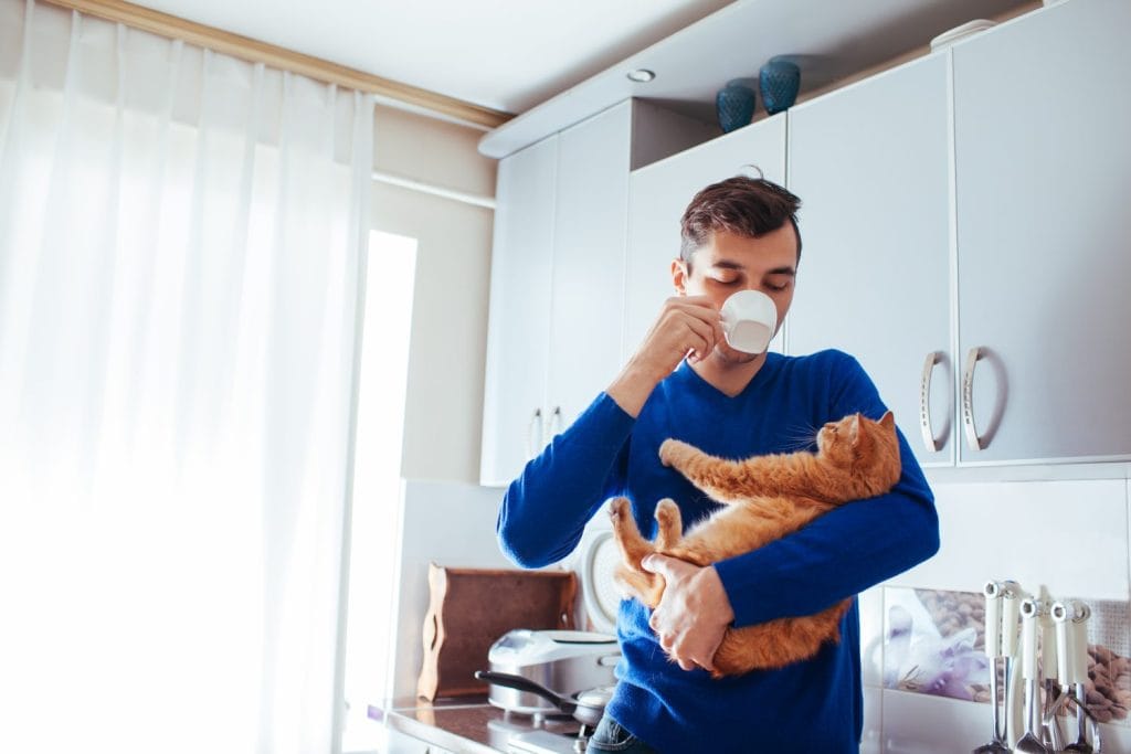 Portrait of handsome young man holding cat and drinking tea on the kitchen.