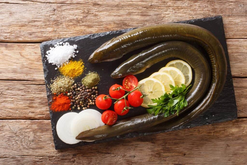 uncooked fresh eel with spices, vegetables and lemon close up on a slate board on the table. horizontal top view from above