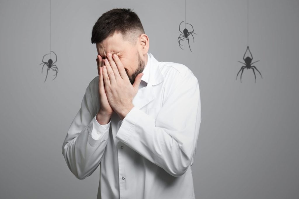 Scared man suffering from panic attack on grey background. Shadows of spiders symbolizing fear and anxiety