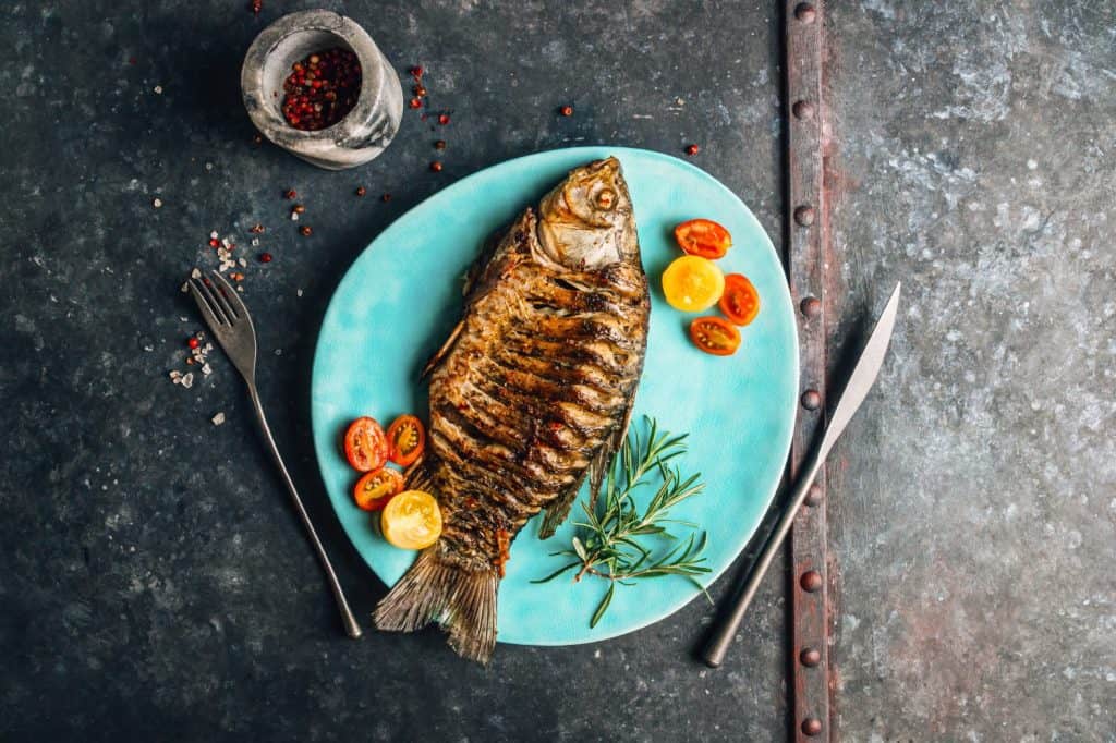 Fried carp fish served on a blue plate over a galvanized background.